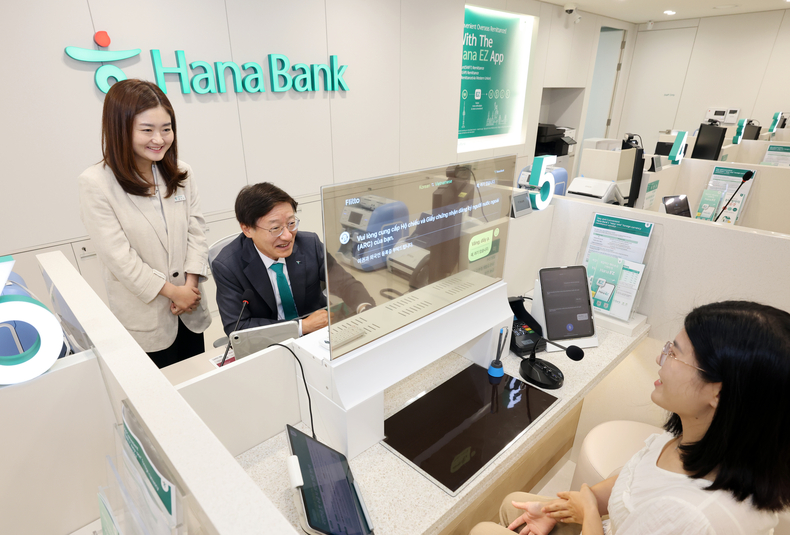 하나은행은 19일 경기도 평택시 평택동에 소재한 외국인 전용 특화점포 '평택외국인센터점'을 개점했다. 이승열 하나은행장(가운데)이 실시간 다국어 통번역 시스템이 설치된 창구에 앉아 투명디스플레이를 통해 외국인 손님을 응대하고 있다.(사진=하나은행)